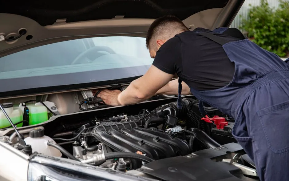 Mécanicien penché sous le capot d’une voiture au garage